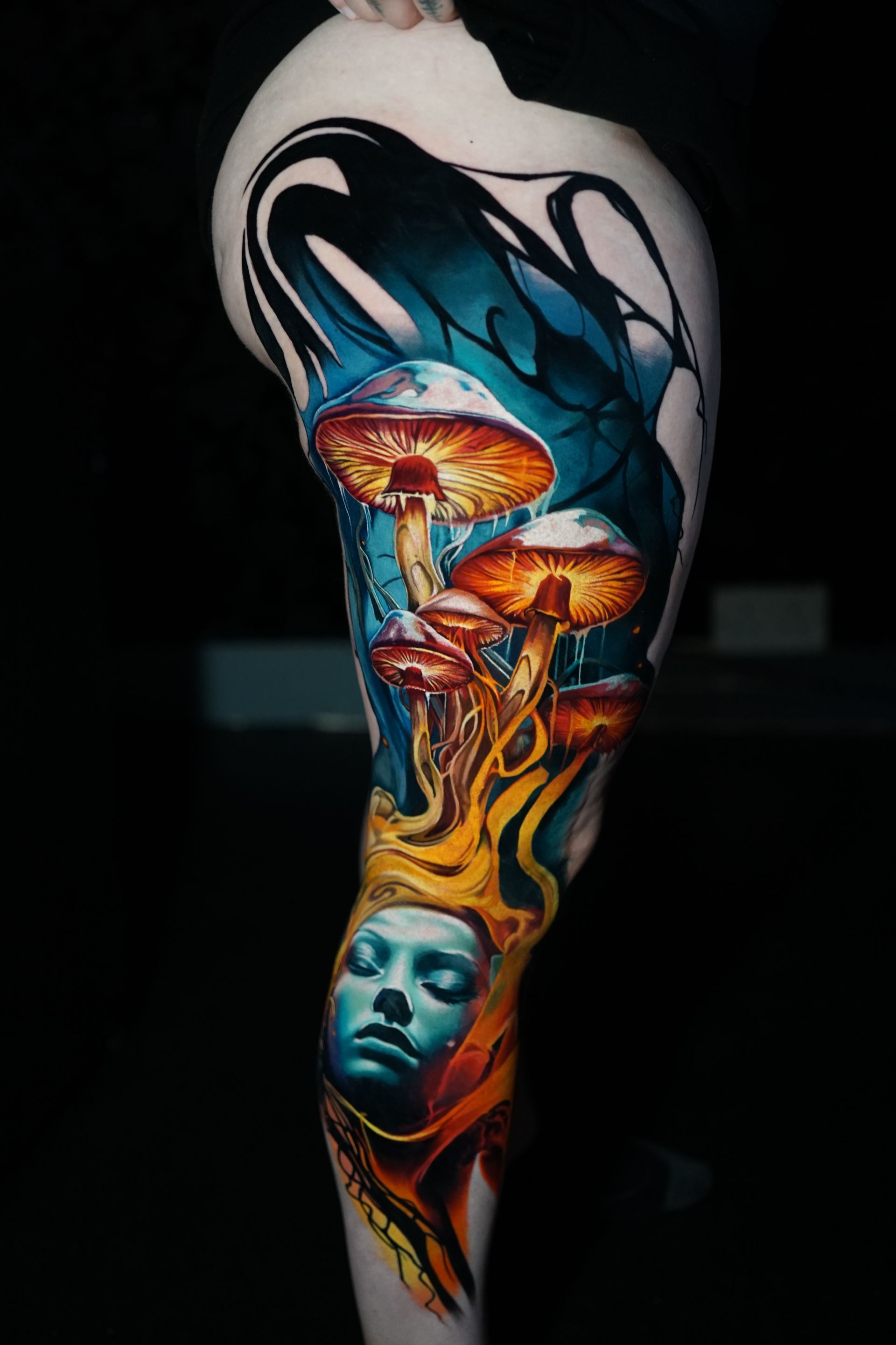 A tattoo of a woman 's face and mushrooms on a leg