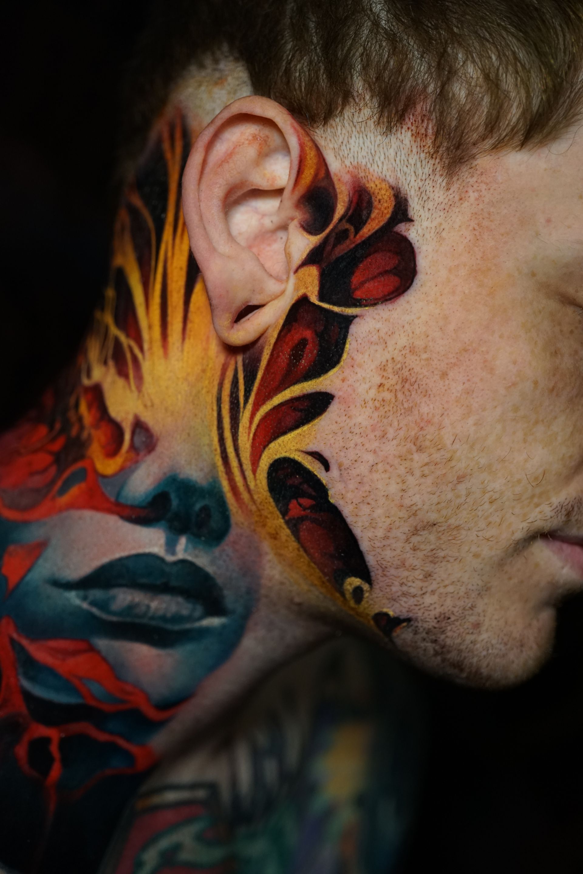 A man has a colorful tattoo on his face and neck.
