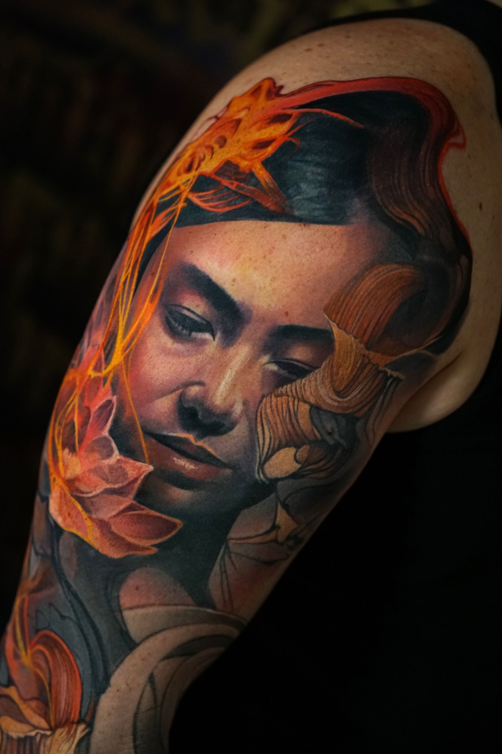 A woman has a tattoo of a woman 's face and flowers on her arm.