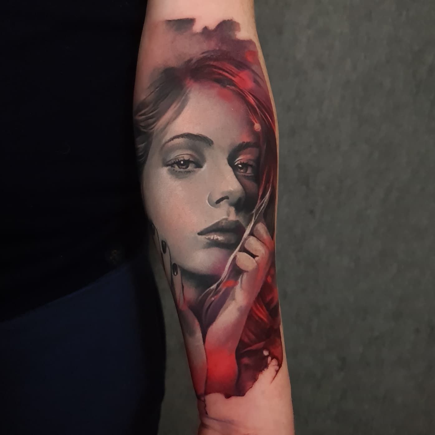 A woman with red hair has a tattoo of her face on her forearm.