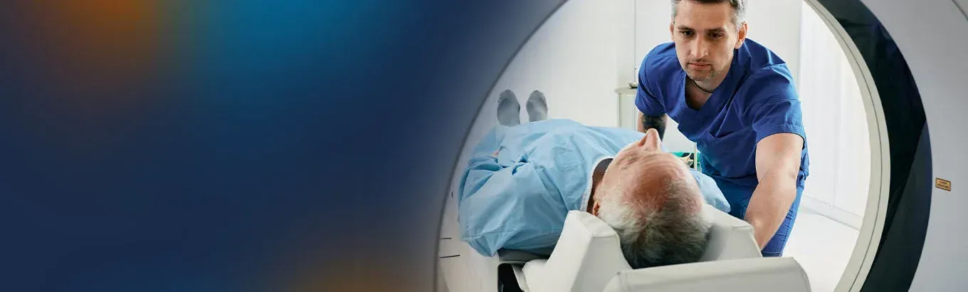Man in medical scrubs pushing a patient on a gurney into a CT scanner.
