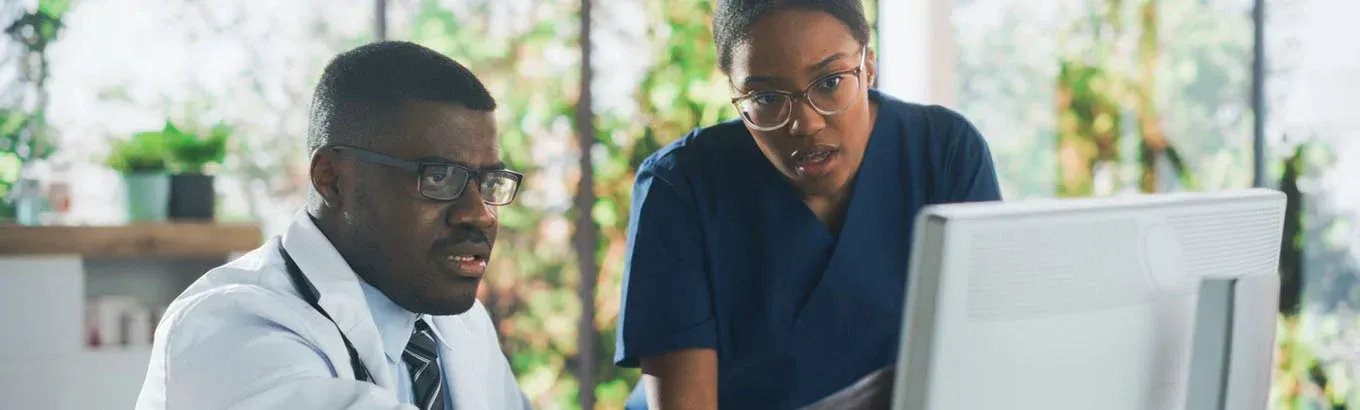 Two healthcare workers looking at a computer monitor in an office with plants.