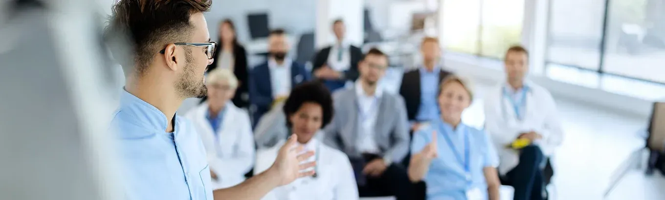 A speaker presents to a diverse group of professionals in a bright, modern office meeting space.