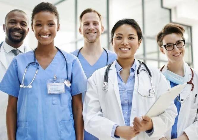 Group of healthcare professionals smiling in a hospital setting, some wearing scrubs and white coats.