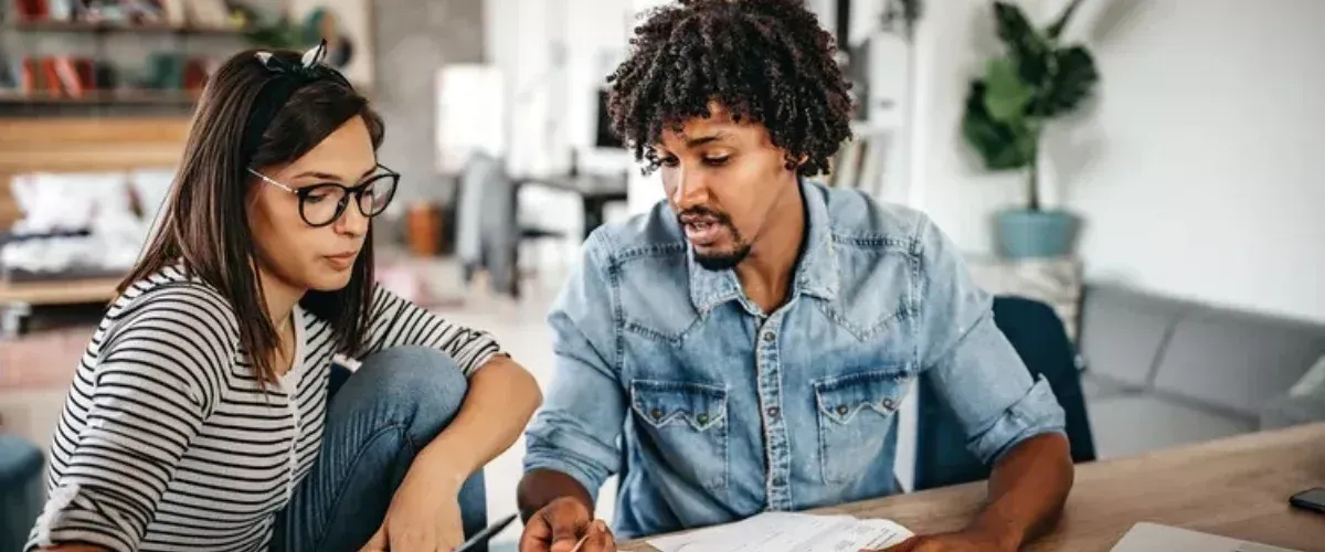 Woman and man looking at papers together, indoors. The man gestures while speaking.