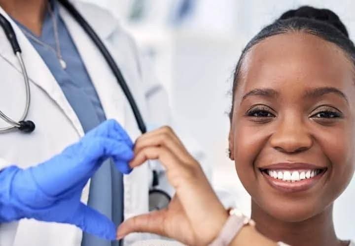 Doctor making a heart shape with hands near a smiling patient in a medical setting.