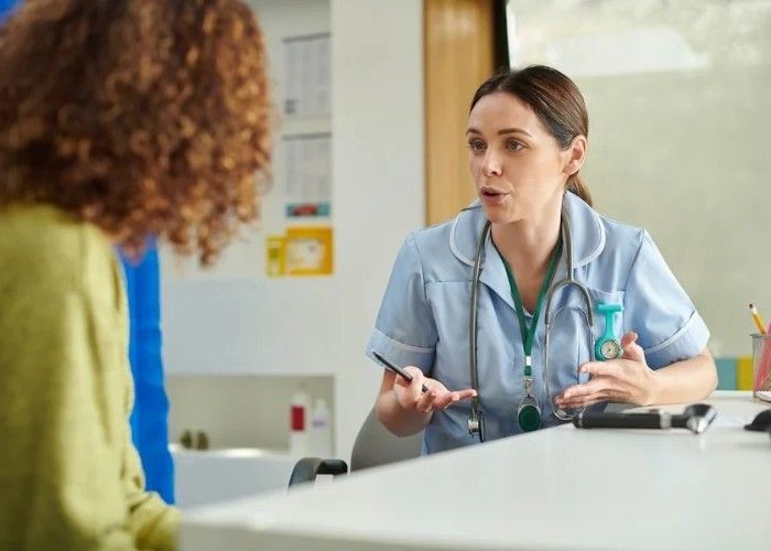 Nurse in blue scrubs talking to a patient, hospital setting.