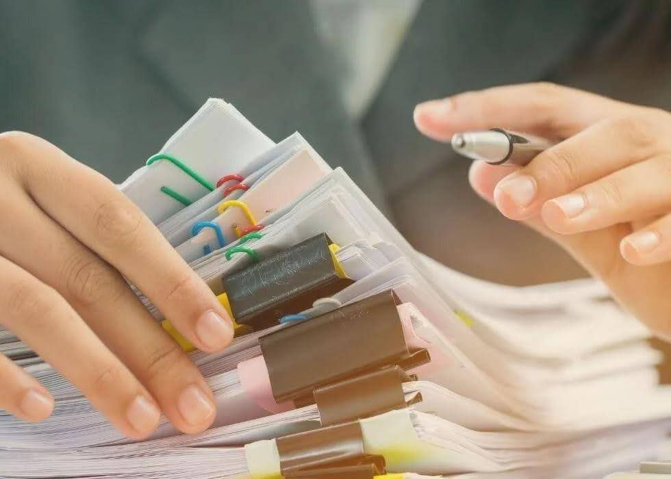 Hands holding a stack of papers, with a pen, preparing to review documents.