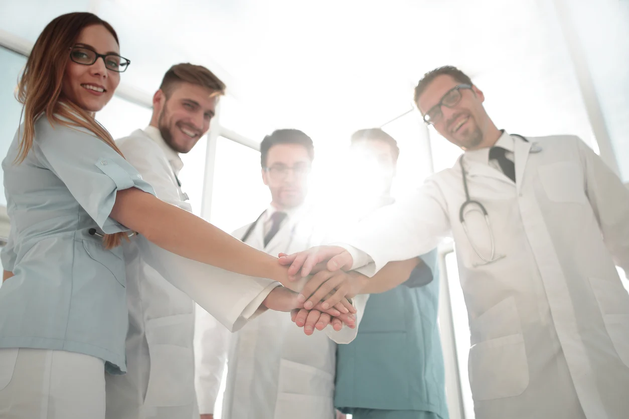 Medical team with hands stacked in a show of unity, wearing white coats and scrubs.