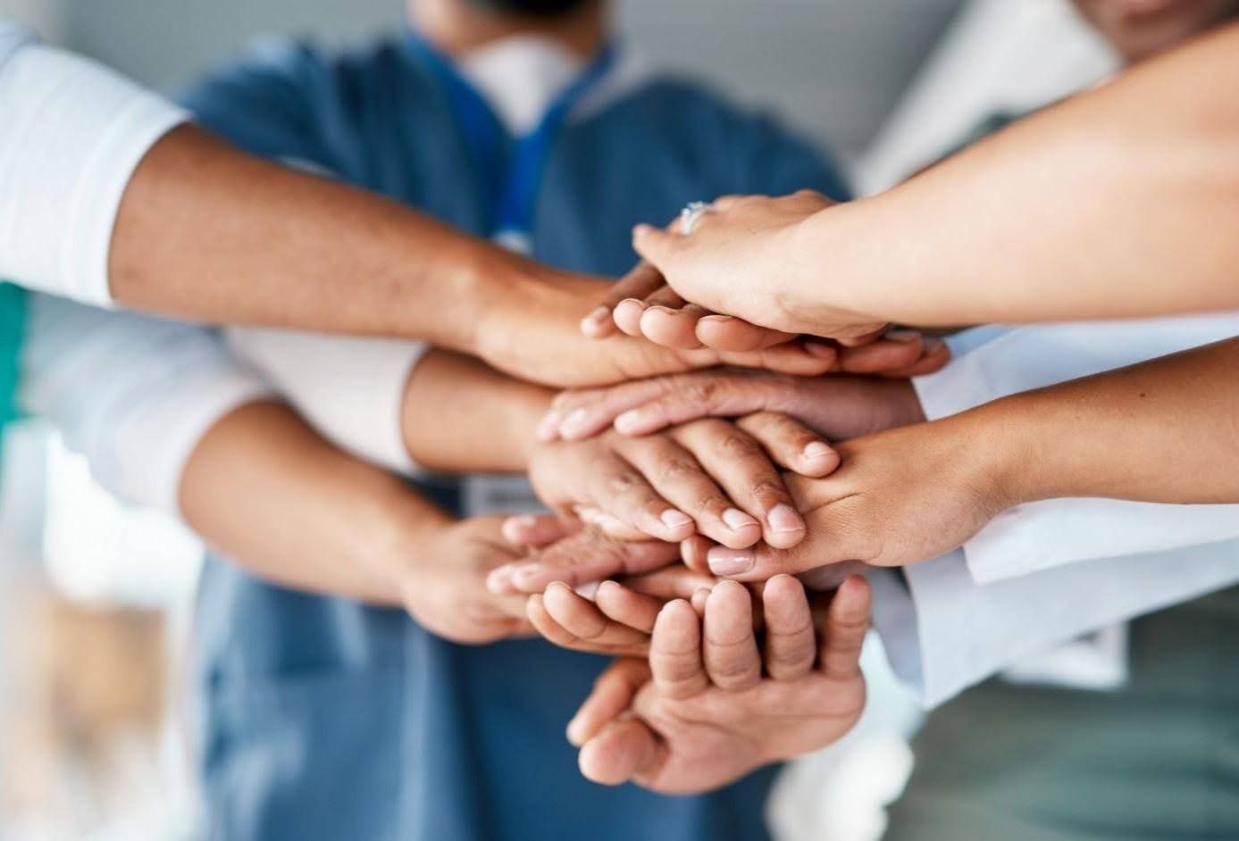 Team of healthcare workers with hands stacked together in unity.