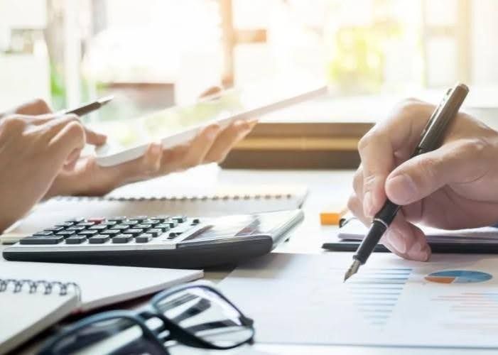 People analyzing financial documents with calculator, pen, and notebooks on a desk.