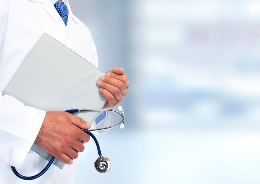 Doctor in white coat, holding a medical chart and stethoscope, blurred background.