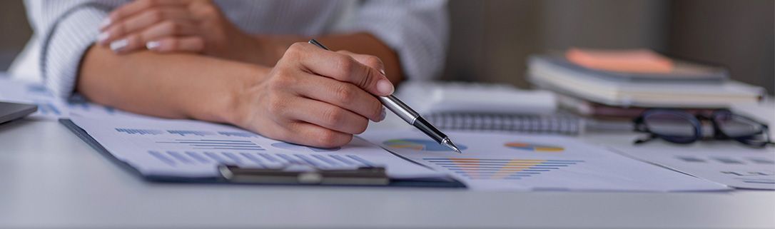 Close-up of hands pointing to a colorful chart on a document at a desk with glasses and notebooks in the background.