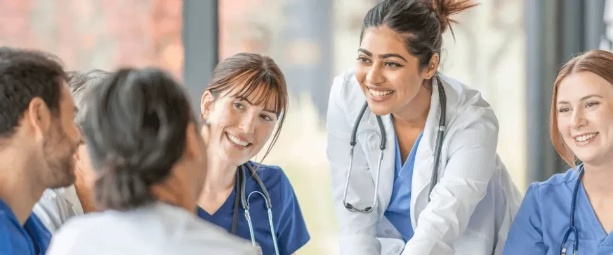 Three medical professionals smiling during a discussion. Two are wearing scrubs, one has a lab coat.