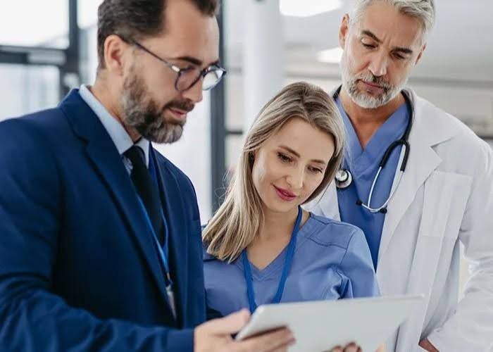 Man in suit, nurse, and doctor looking at tablet in a bright office.