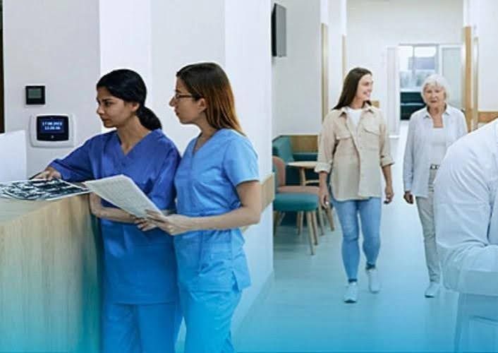 Two nurses at a hospital reception desk; two patients walking in a hallway.