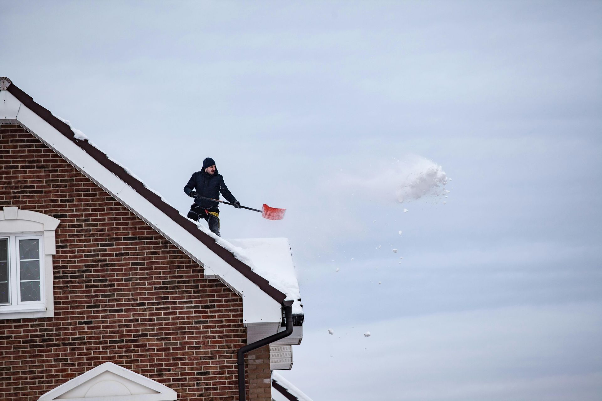 Man shoveling snow off a brick house roof.
