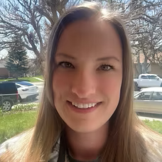 Woman with long blonde hair smiles at the camera. A sunny outdoor setting is in the background.