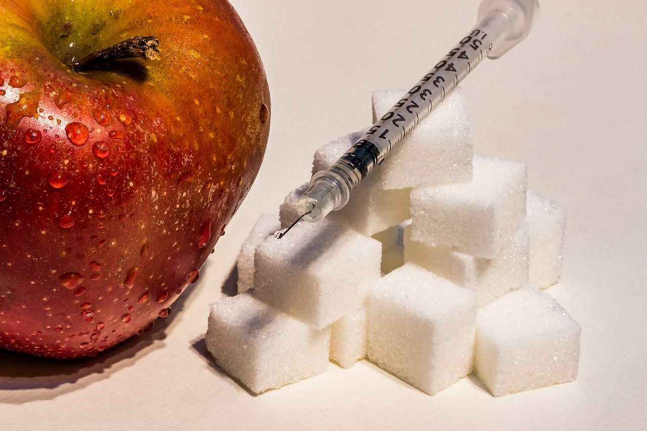 A syringe rests on a pile of sugar cubes next to an apple