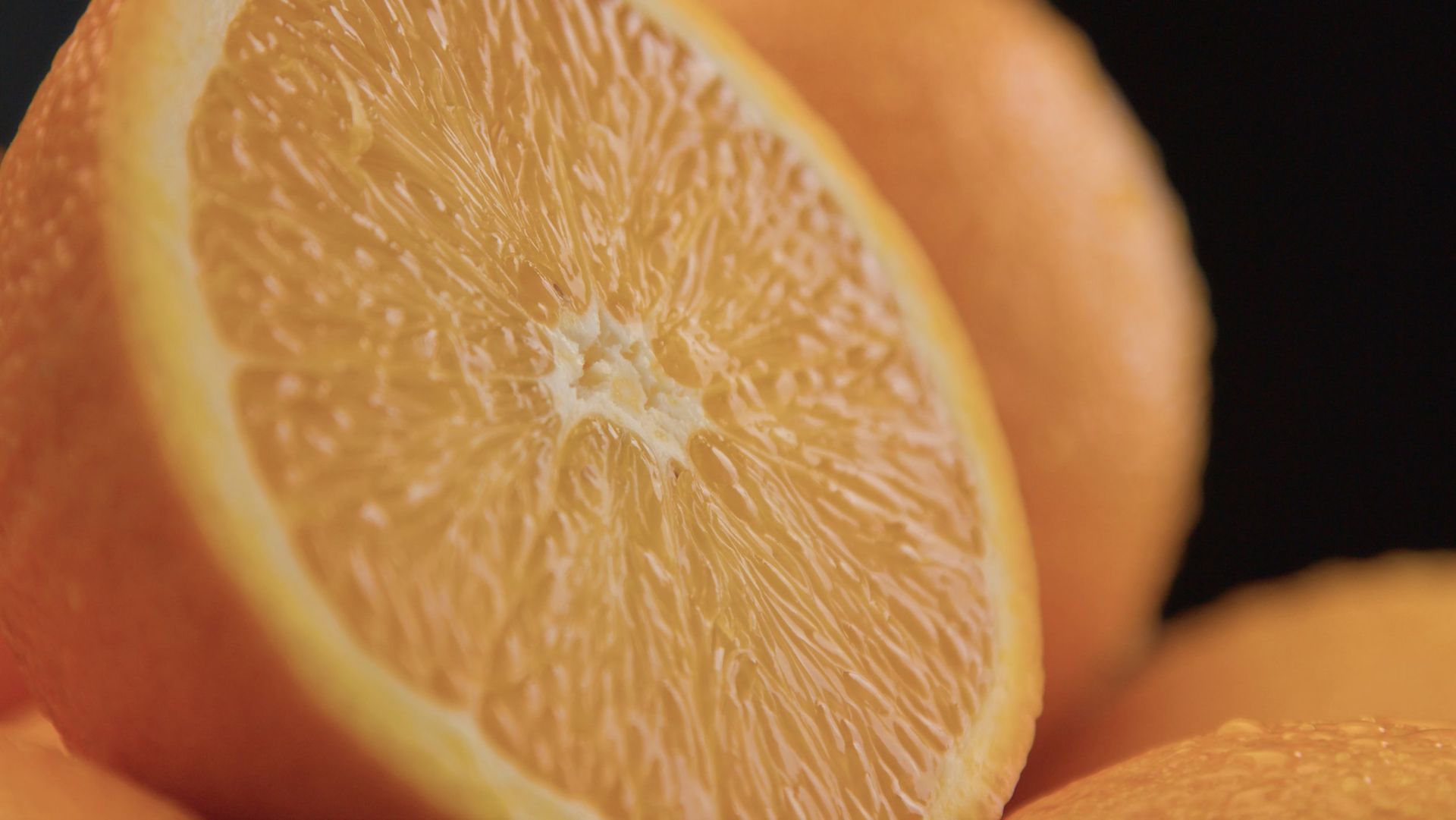 A close up of a sliced orange on a pile of oranges on a black background.