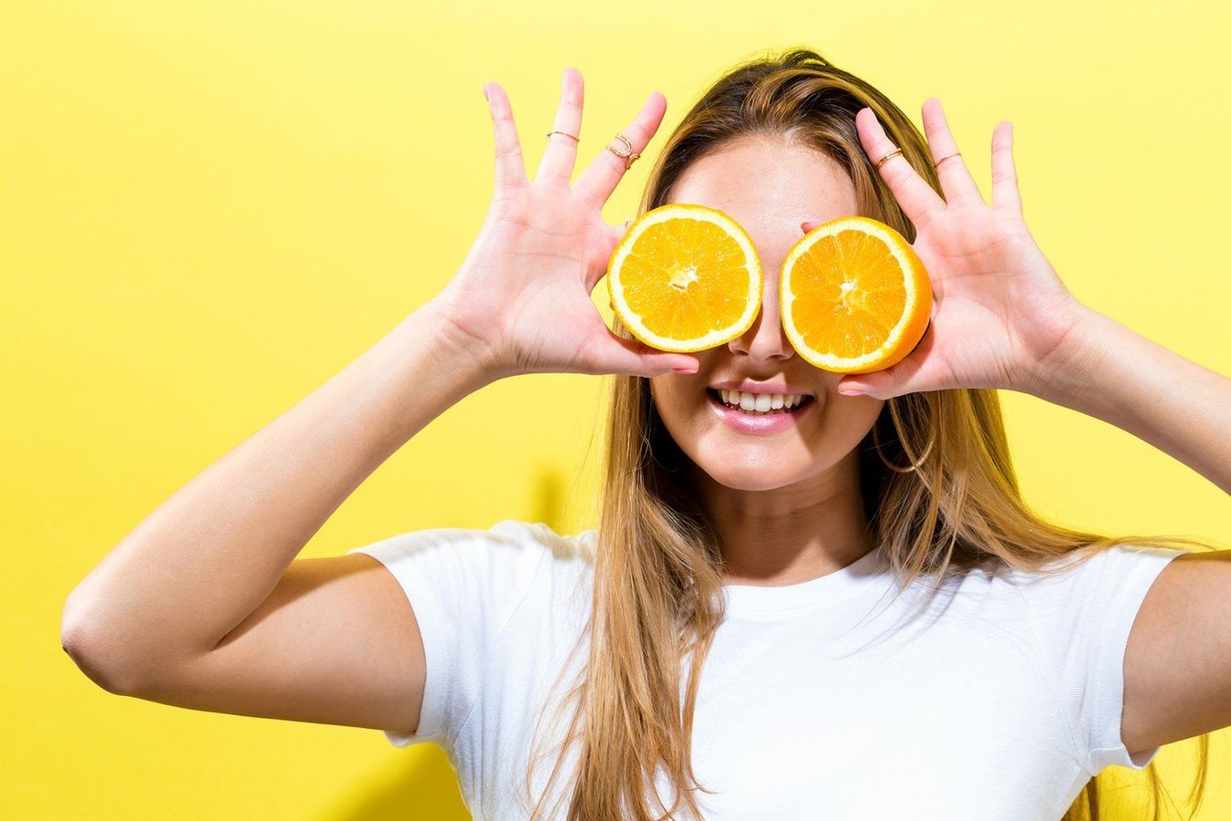 A woman is covering her eyes with slices of orange.