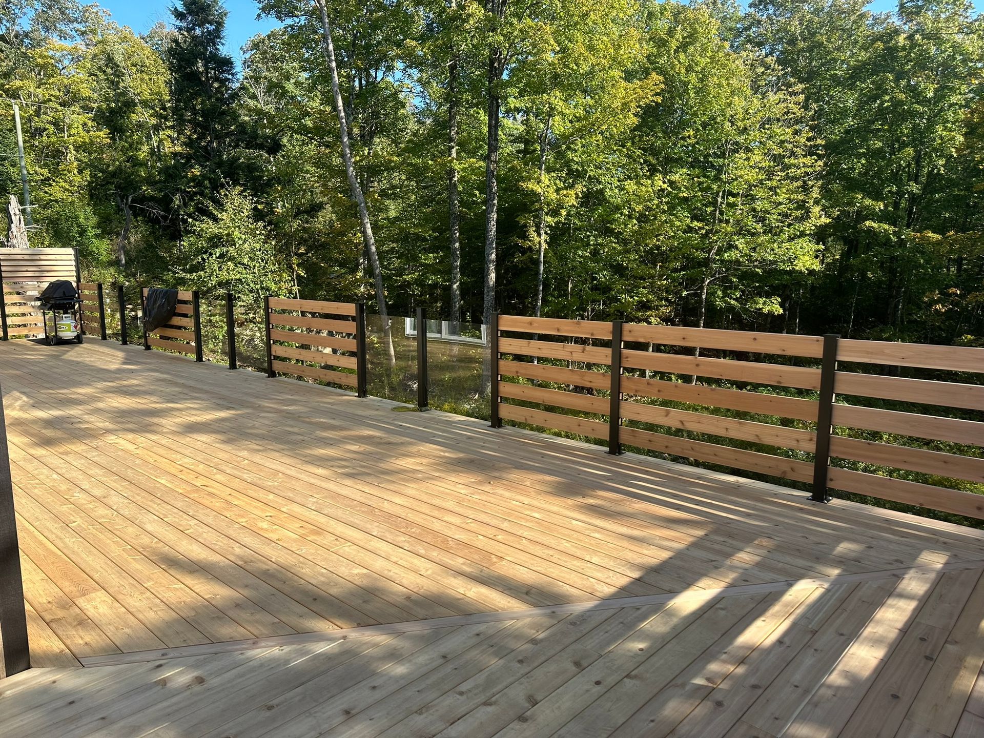 Terrasse en bois avec clôture horizontale en bois et poteaux noirs ; arbres en arrière-plan.