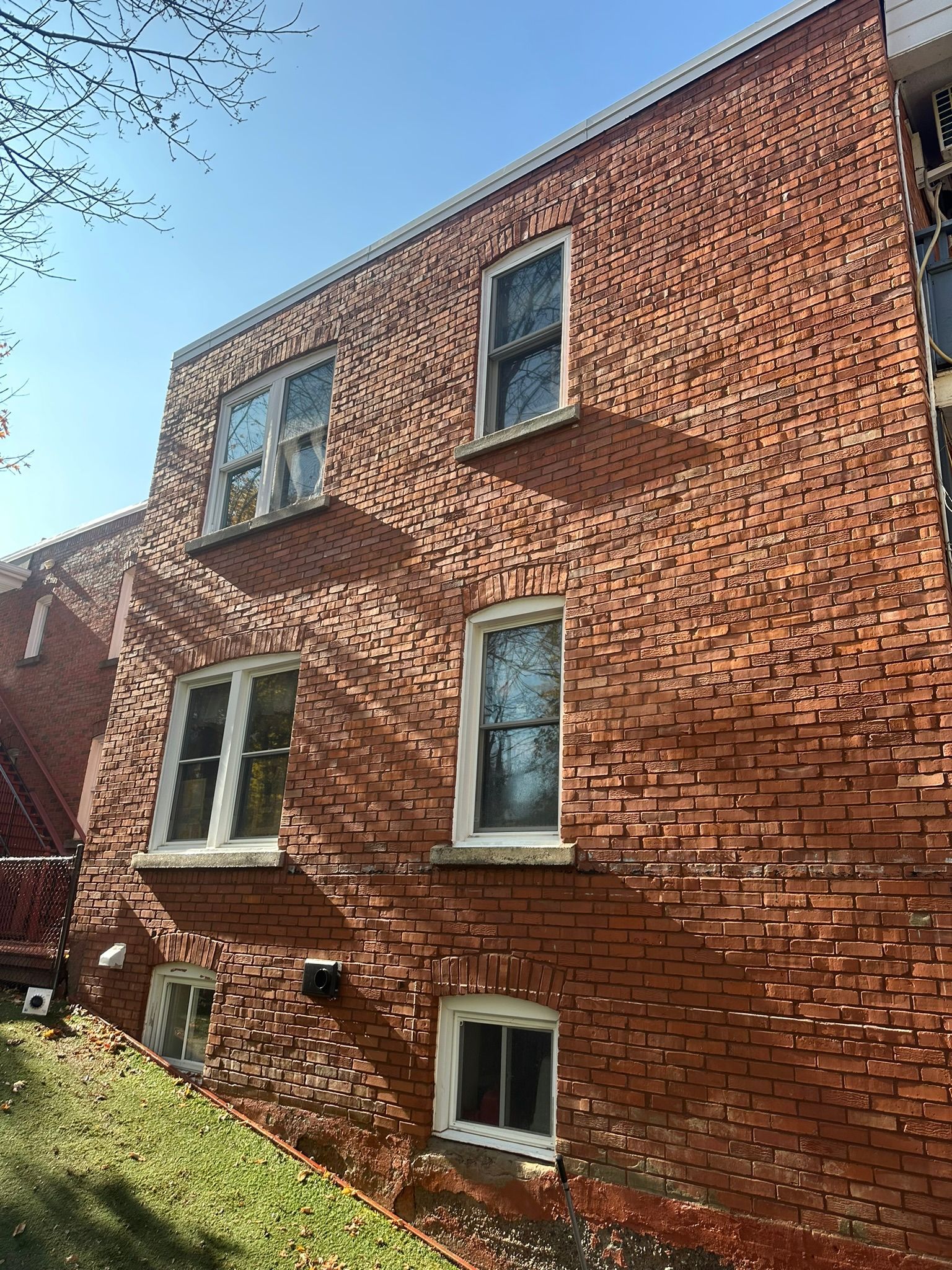 Bâtiment en briques rouges aux multiples fenêtres à encadrement blanc, se détachant sur un ciel d'un bleu éclatant.