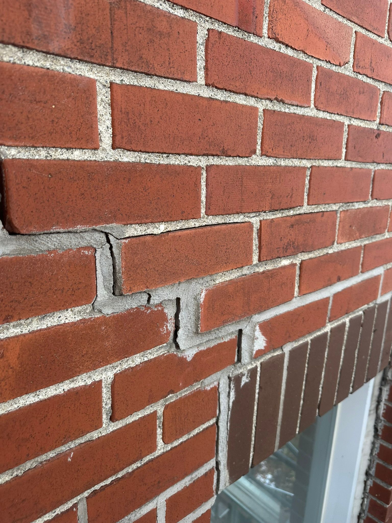 Mur de briques présentant une importante fissure horizontale, laissant apparaître un mortier détérioré.