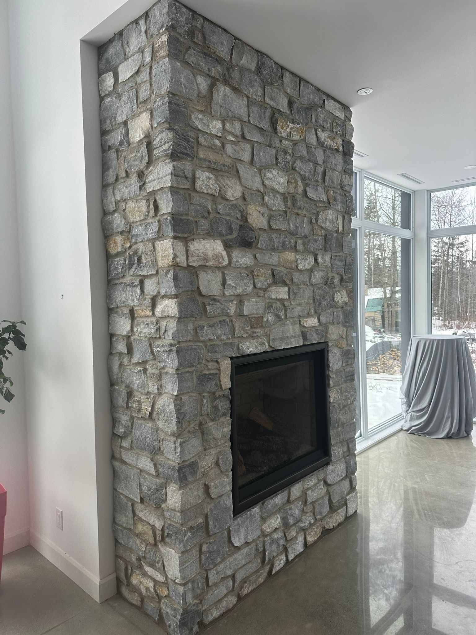 Cheminée revêtue de pierre avec une ouverture encadrée de noir dans une pièce lumineuse et moderne.