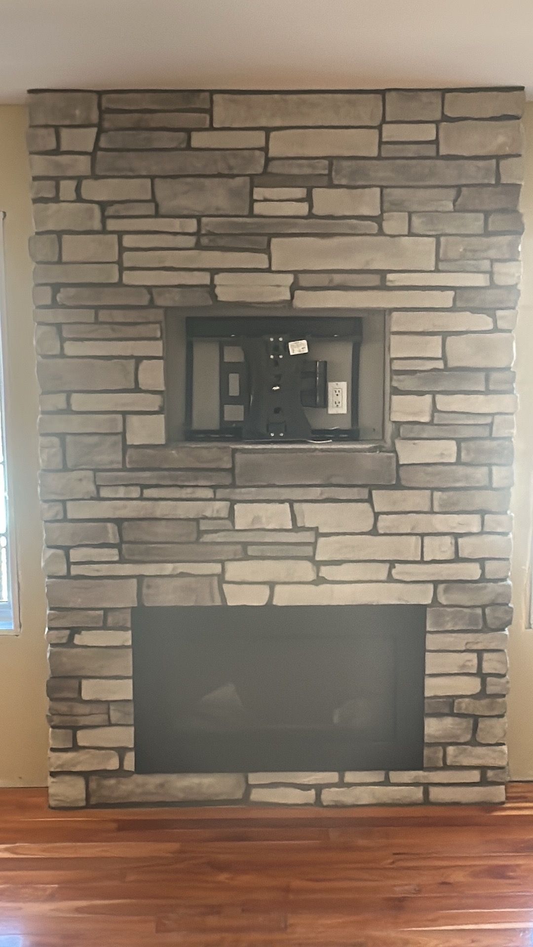 Cheminée en pierre avec support TV encastré au-dessus du foyer, sur un parquet.