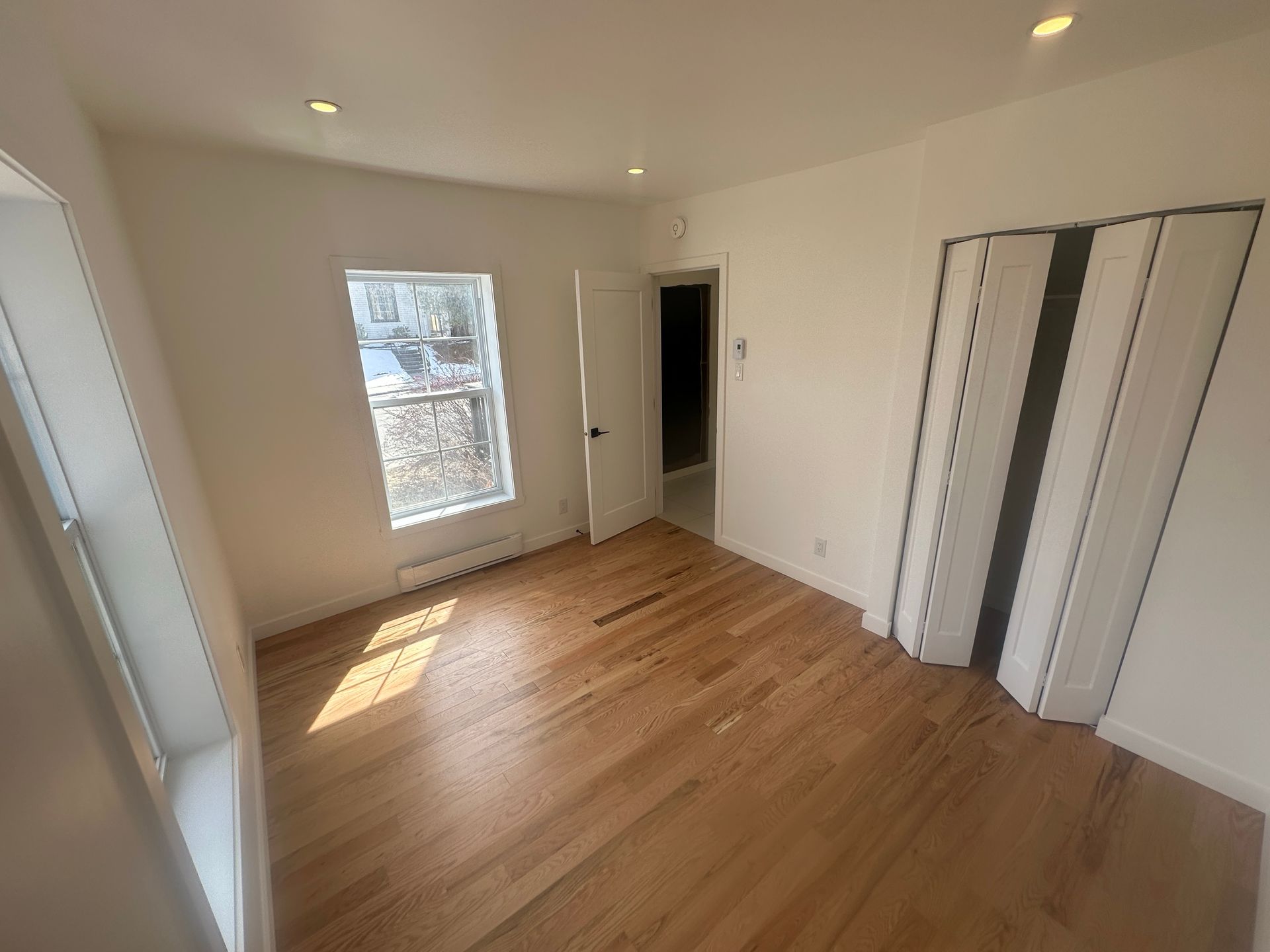 Pièce vide avec parquet, une fenêtre, un placard et une porte.