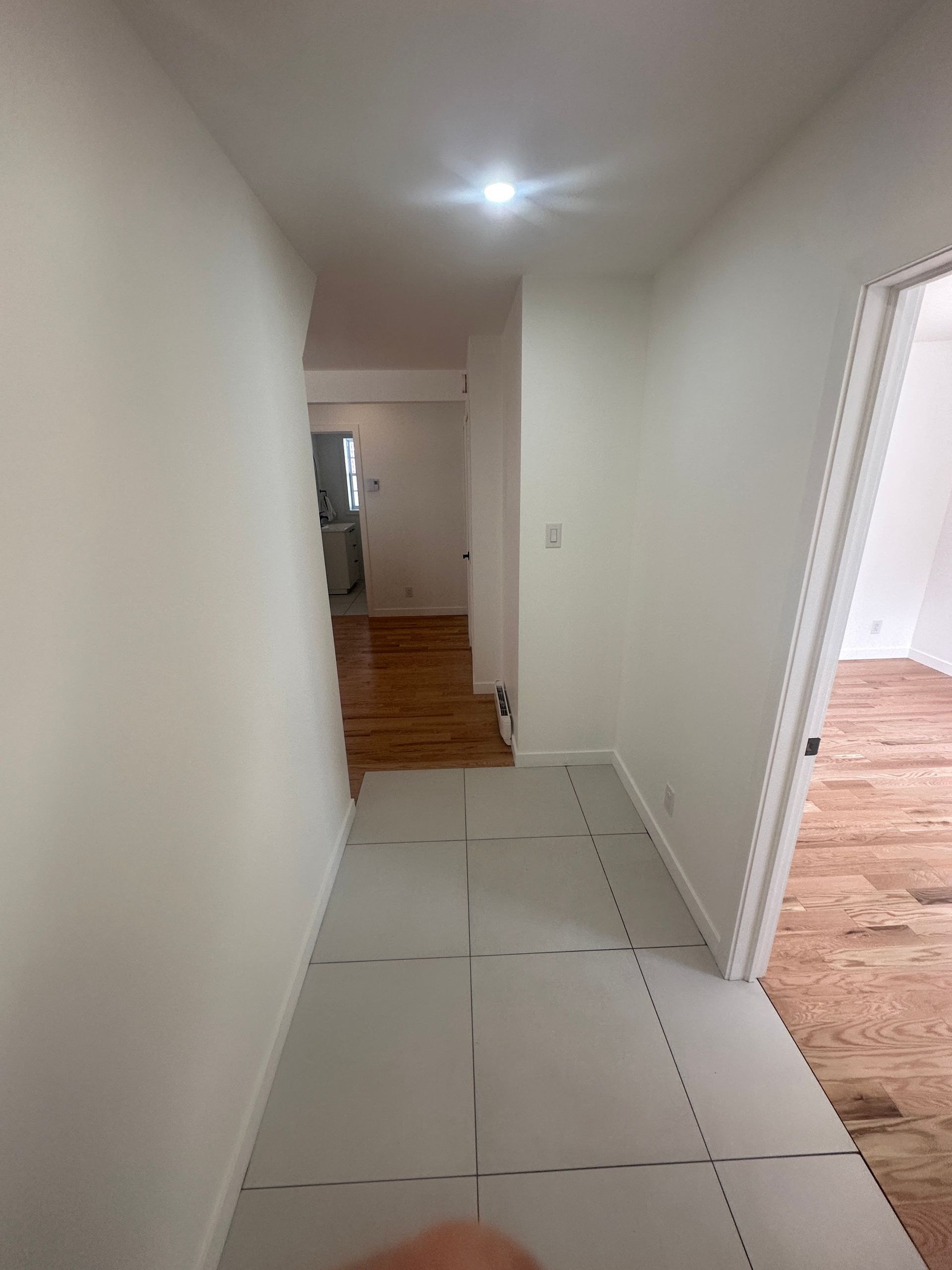 Couloir étroit aux murs et au sol blancs ; une porte à droite, pièce au fond.