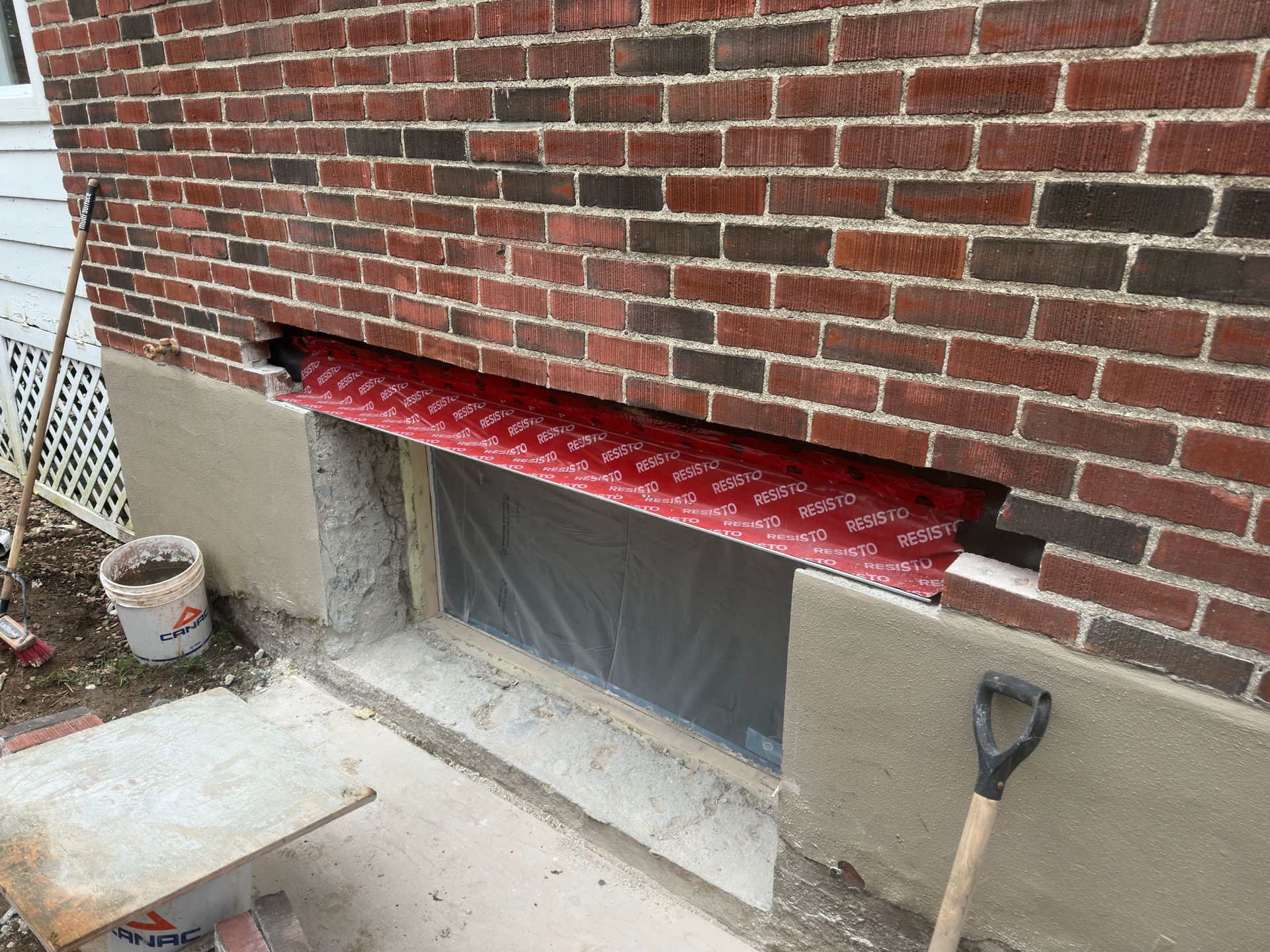 Mur en briques avec ouverture rectangulaire, solin métallique rouge, socle en béton.