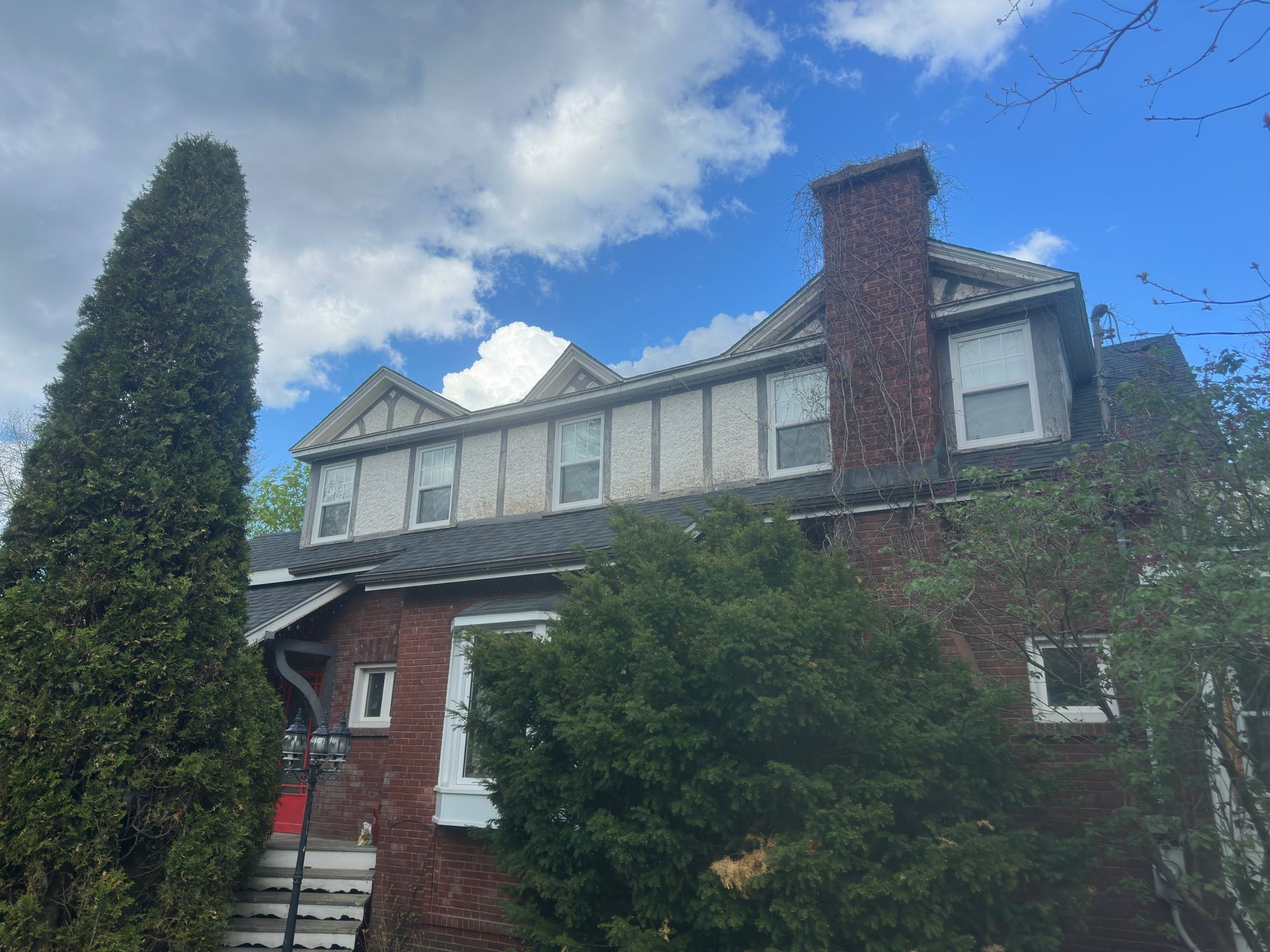 Maison en briques avec une porte rouge, des boiseries blanches et une haute cheminée sous un ciel bleu.