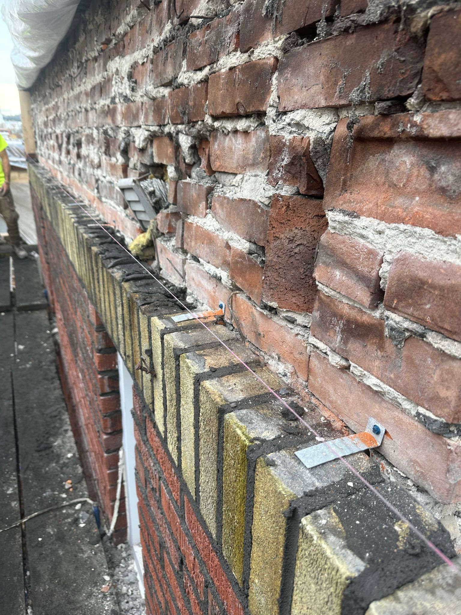 Mur de briques endommagé, probablement en cours de réparation. Les briques sont érodées et le mortier est visible. Une corde est tendue le long du rebord.