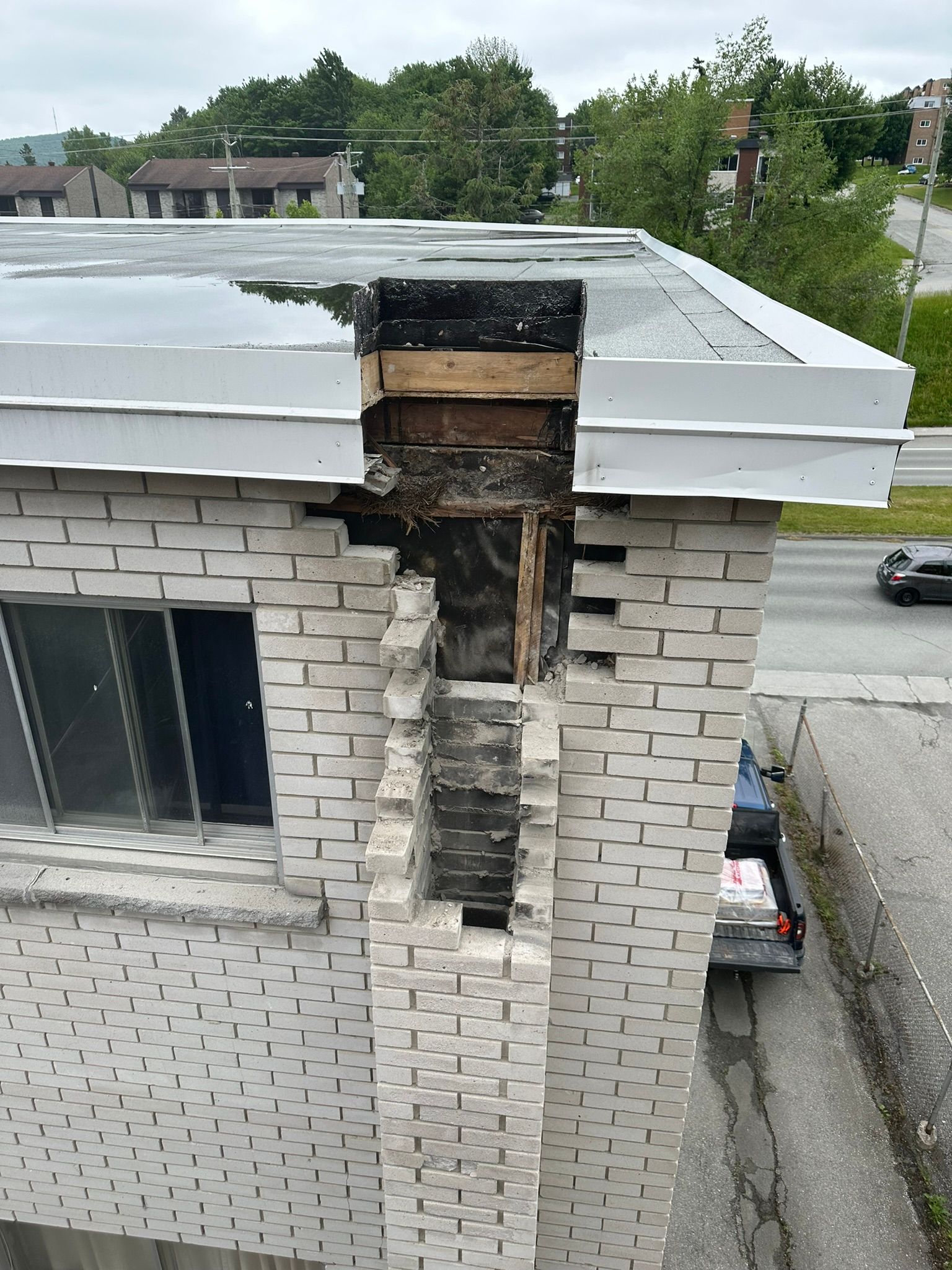 Cheminée en briques endommagée faisant saillie d'un toit plat, laissant apparaître l'intérieur.