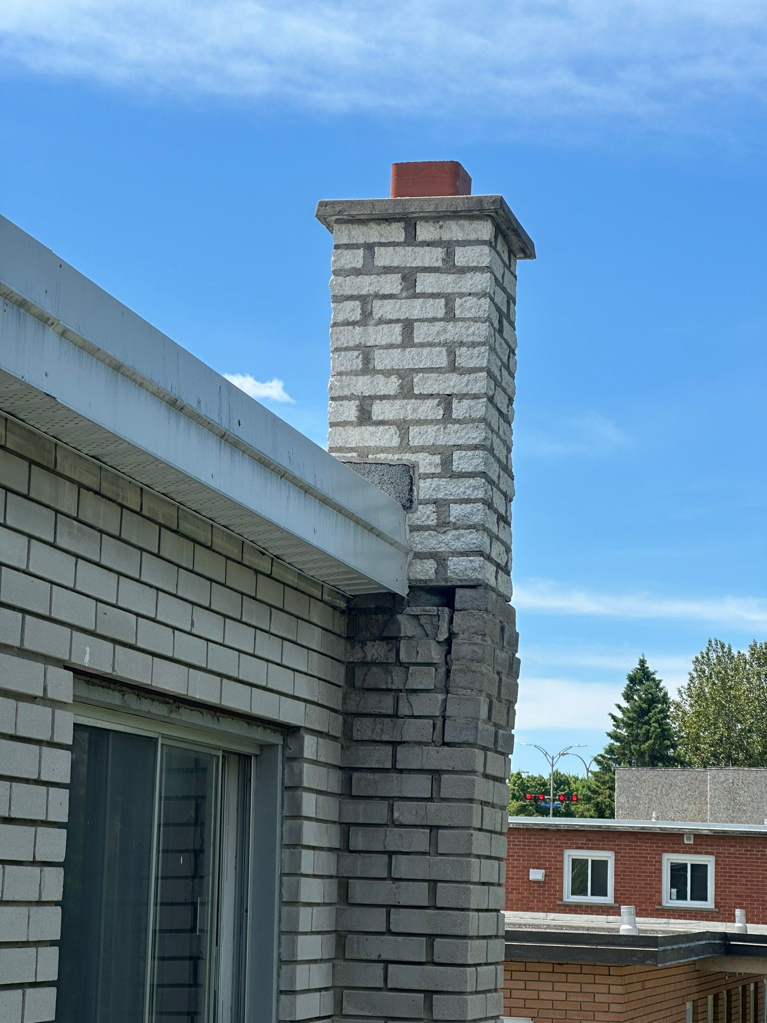 Cheminée en briques sur un bâtiment partiellement endommagé, ciel bleu en arrière-plan.