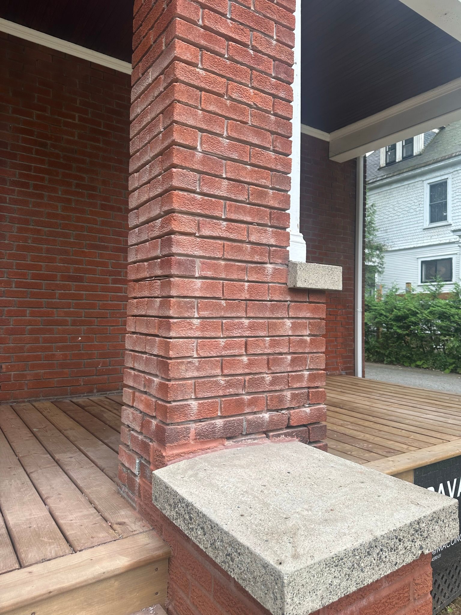 Colonne de porche en briques avec chapiteaux en béton et plancher de porche en bois.