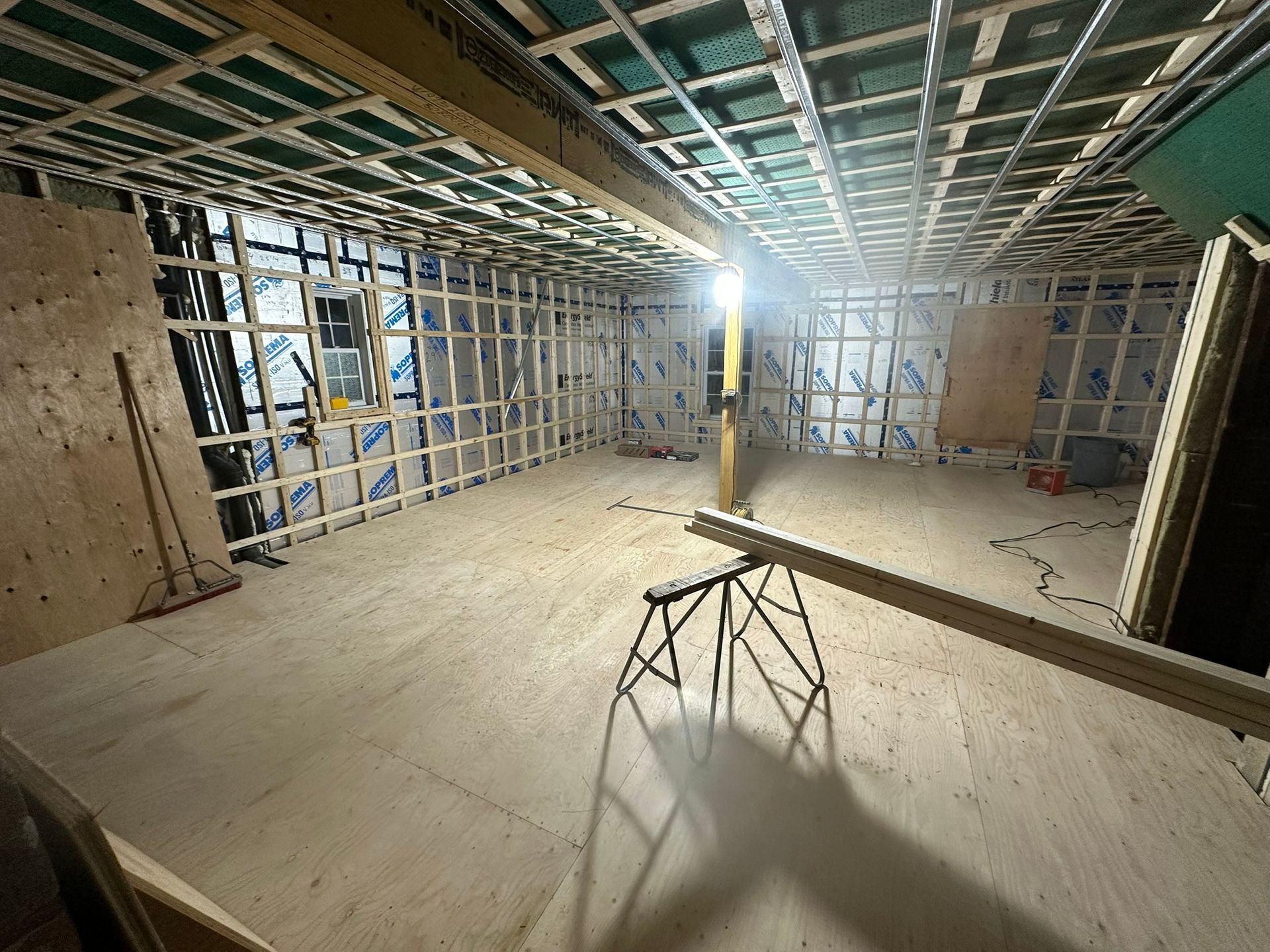 Vue intérieure d'une pièce en construction avec charpente en bois apparente et plancher en contreplaqué.