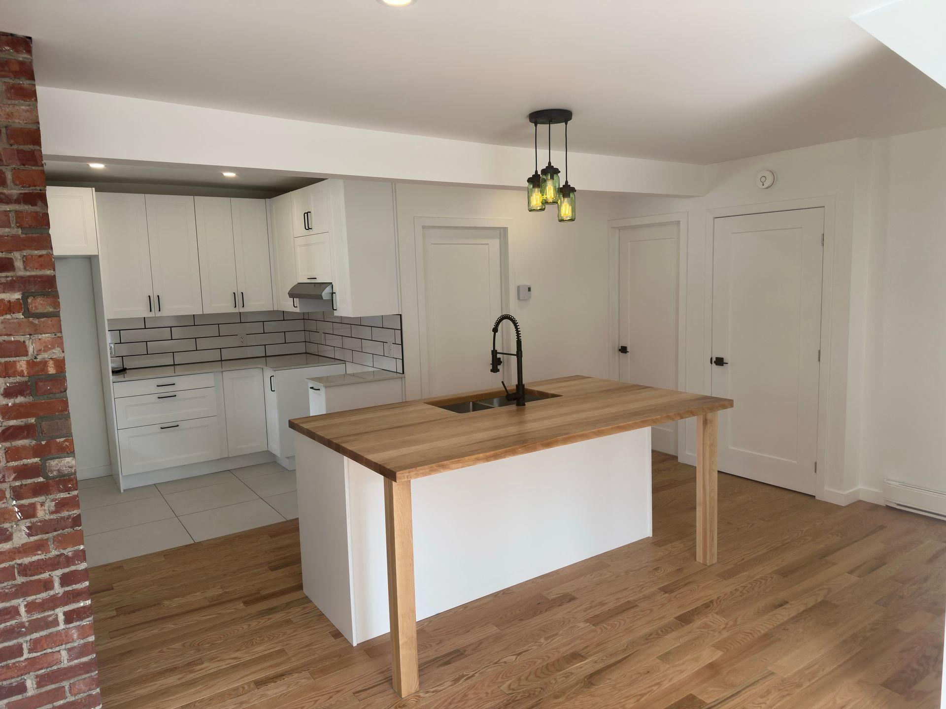 Cuisine moderne avec armoires blanches, îlot central avec comptoir en bois et mur d'accent en briques.