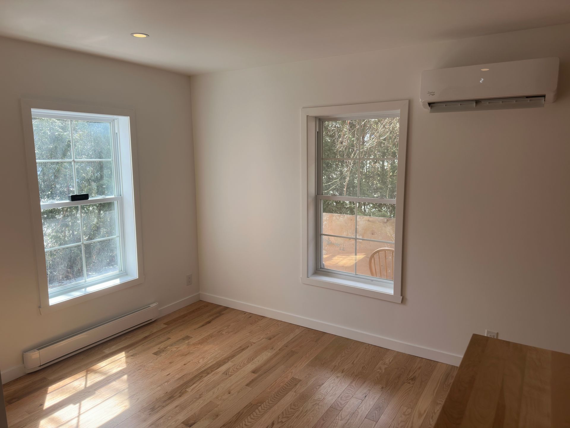 Pièce vide avec parquet, deux fenêtres et un climatiseur mural.