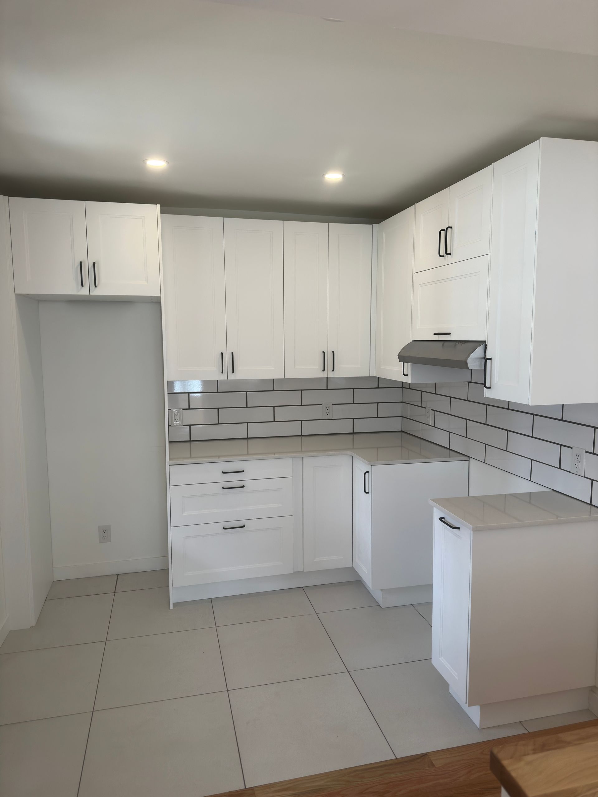 Cuisine blanche avec placards, crédence grise et sol carrelé blanc.