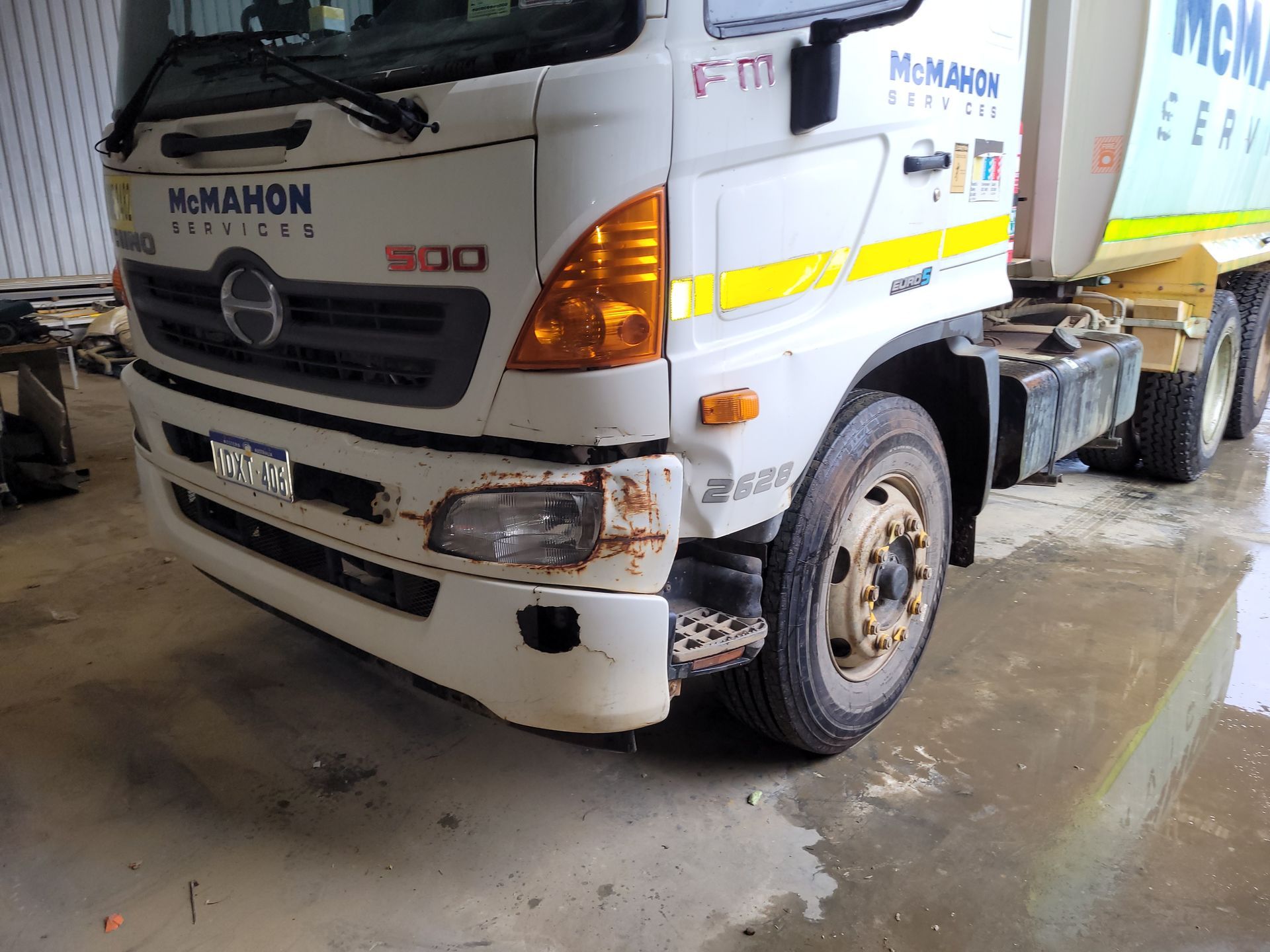 A white truck with a yellow stripe on the side is parked in a garage.