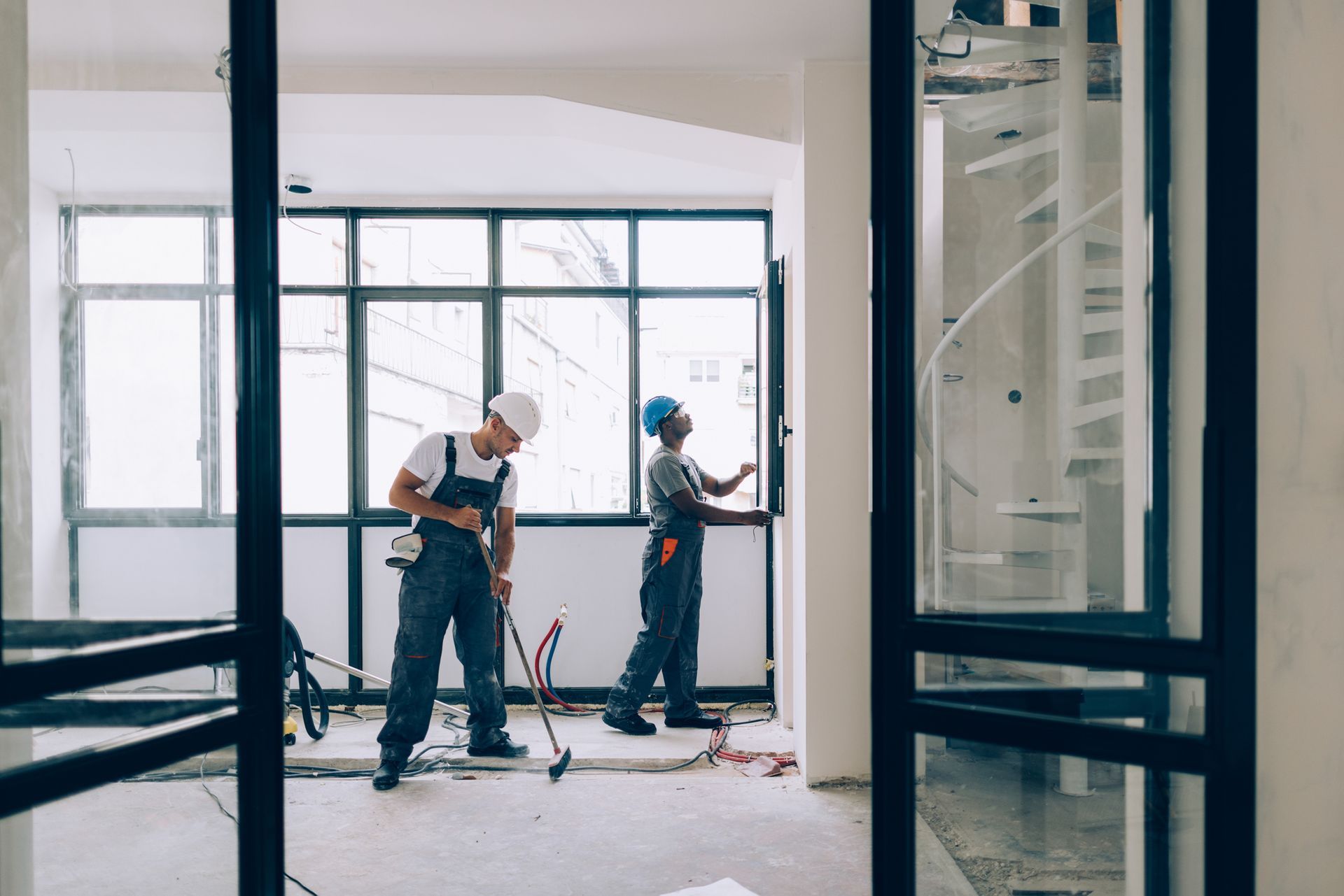 Two construction workers are working in an empty room.