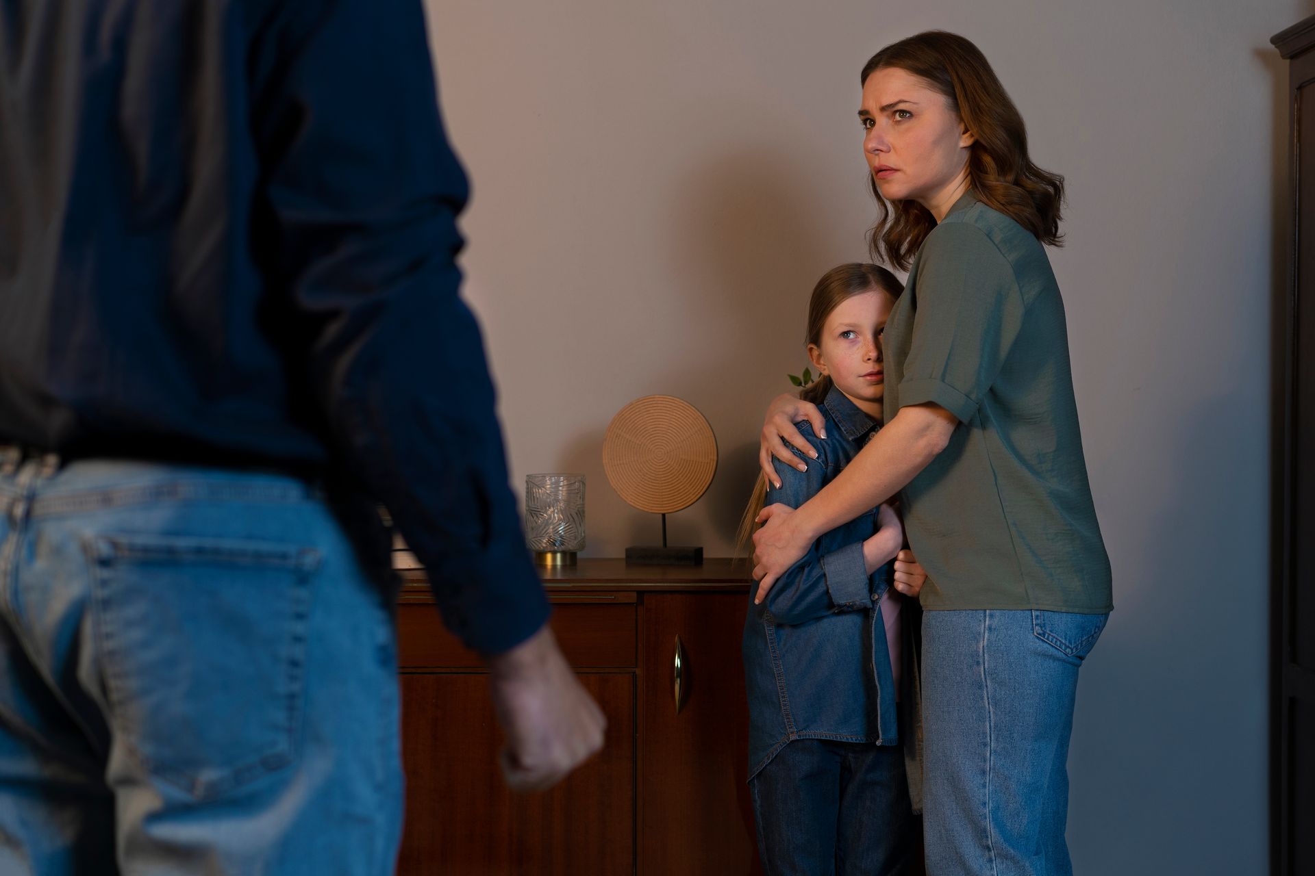 Man faces family. Woman and child look worried, indoors.