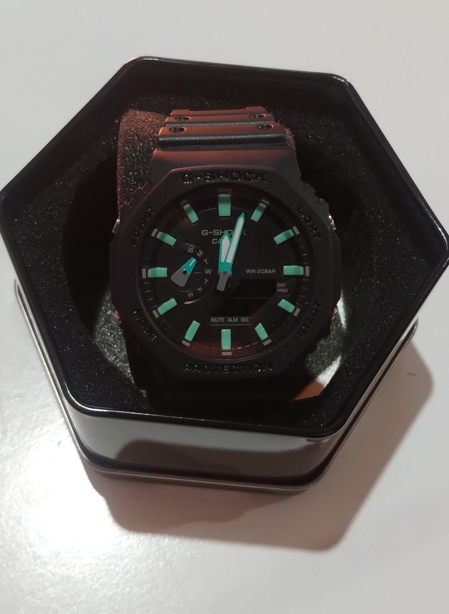 Un reloj negro con manecillas verdes está en una caja negra
