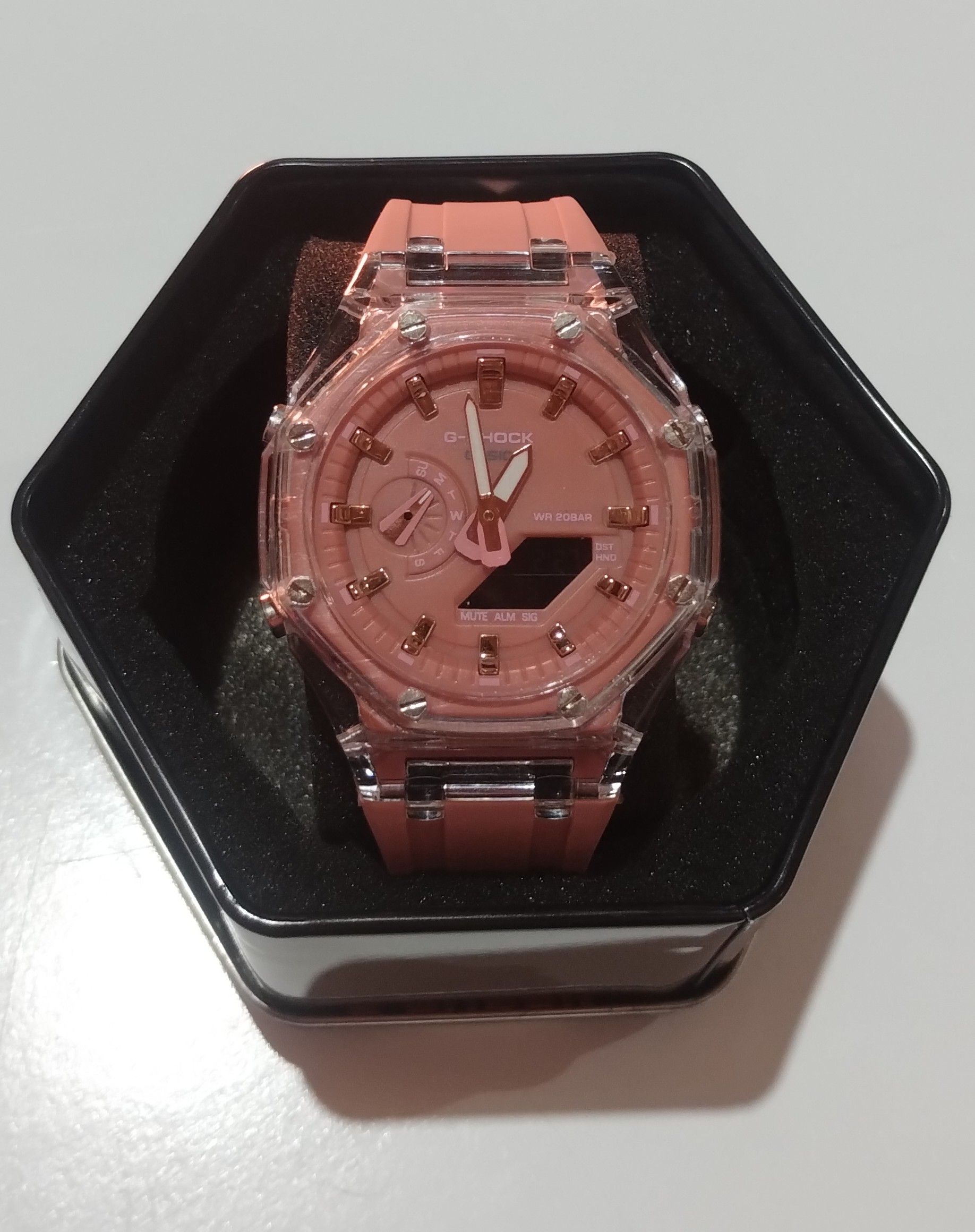 Un reloj rosa con la cara transparente está en una caja negra.