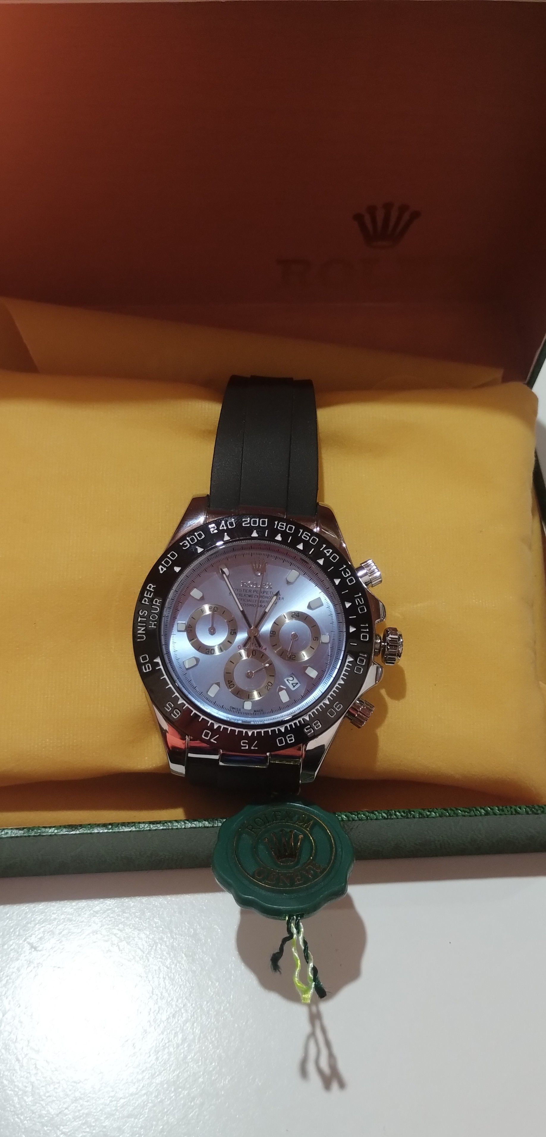 Un reloj Rolex está en una caja amarilla sobre una mesa.