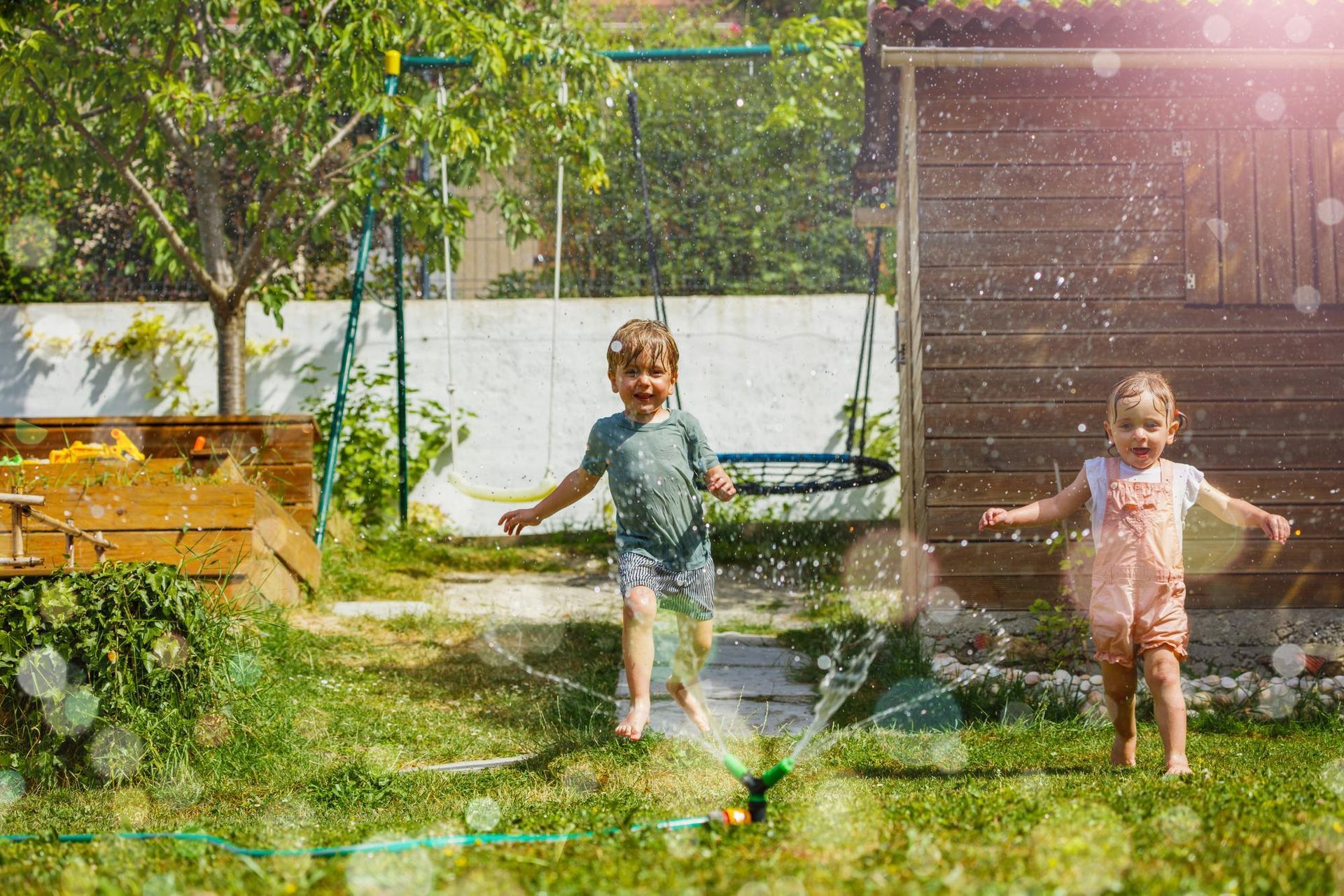 A boy and a girl are playing with a sprinkler in a backyard.