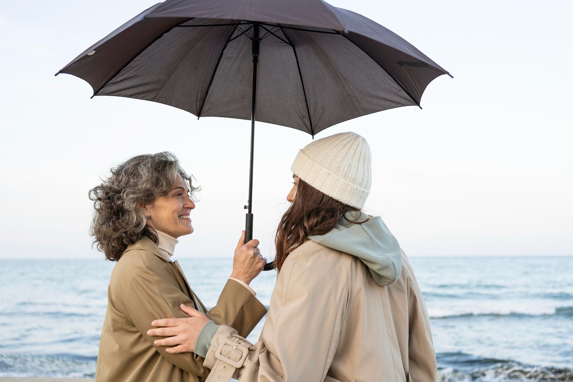 Two women are standing under an umbrella on the beach.
